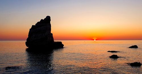 Rock formation in sea against sky during sunset