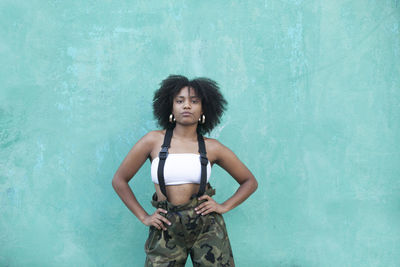 Portrait of young woman with curly hair standing against wall