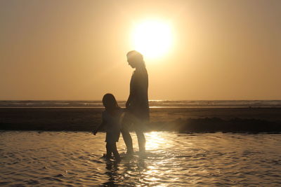 Mother and daughter walking on shore during sunset