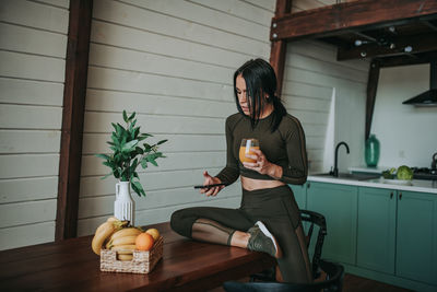 Woman using phone while drinking juice in kitchen at home