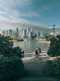 People riding bicycle by river against buildings in city