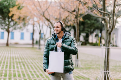 Mid adult man holding bag looking away while standing outdoors