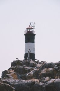 Lighthouse on rock by building against sky