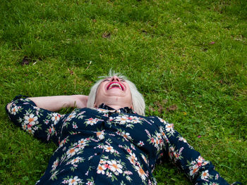 High angle view of cheerful mature woman lying on grassy field