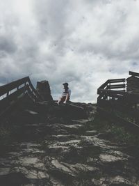Low angle view of woman sitting on hill against cloudy sky