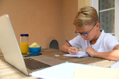 Student doing homework with books and laptop. boy writing sitting at the table. school concept.