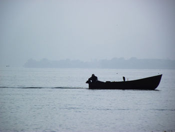 Silhouette man on boat in sea against sky