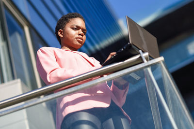 Low angle view of woman using laptop on railing while standing in balcony