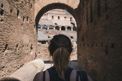 Rear view of woman leaning on stone wall