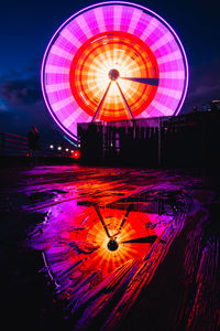 Low angle rainy view of illuminated ferris wheel at night