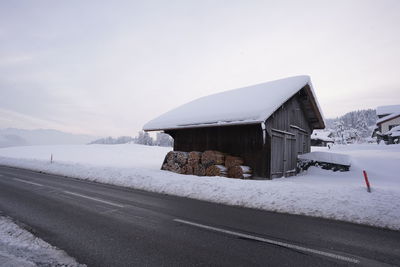 Snow covered road by building against sky