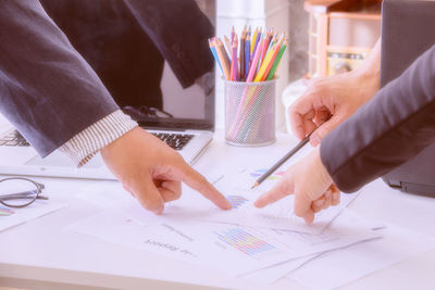 Cropped hands of business people discussing documents on table at office