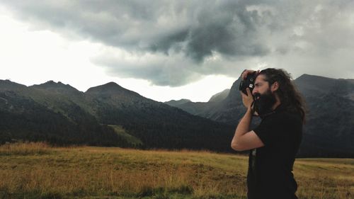 Woman photographing on mountain against sky