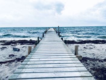 Wooden pier leading towards sea against sky