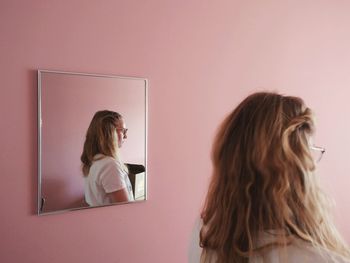 Rear view of woman standing by mirror at home