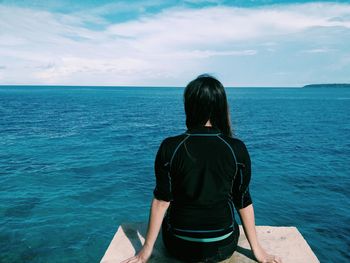 Rear view of woman standing by sea against sky