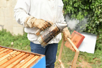 Beekeeper smoking bees with bee smoker at the apiary
