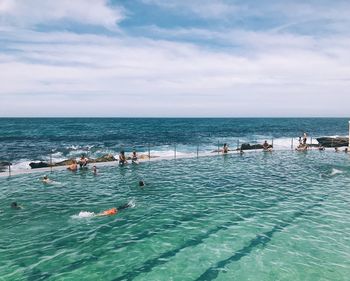 People swimming in pool against sea