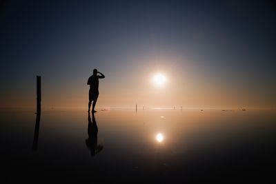 Silhouette man standing in sea against sky during sunset