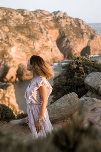 Side view of woman looking away while standing at rock formation