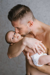 Dad holds his baby in his arms at home and kisses the baby on the cheek