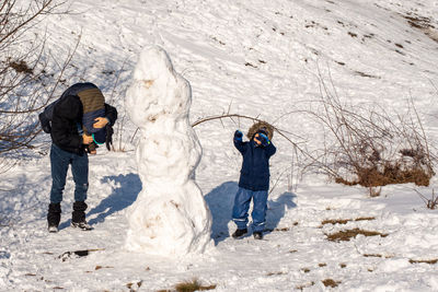 Full length of man and children playing while standing on snow