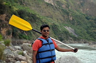 Young man with oar standing by river