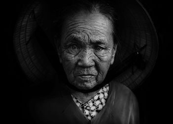 Close-up portrait of serious senior woman against black background