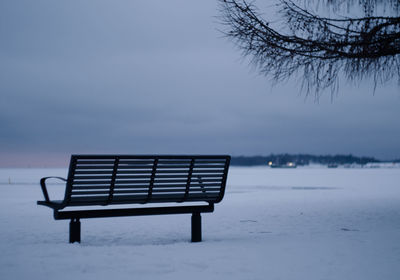 Empty bench on snow covered land against sky