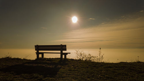 Bench on field against sky during sunset