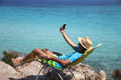 Portrait of a handsome man lying on a deckchair and and taking selfie. summer vacation concept.