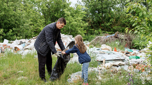 Full length of father and daughter collecting garbage outdoors