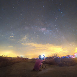 Rear view of woman standing on field against sky at night