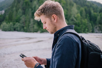 Side view of young man using mobile phone while standing on land