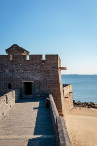 Built structure by sea against clear blue sky