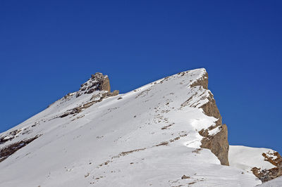 Low angle view of snowcapped mountain against clear blue sky