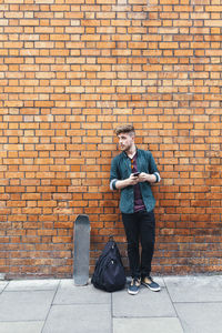 Young skateboarder standing in front of brick wall