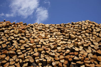 Low angle view of stacked logs against blue sky
