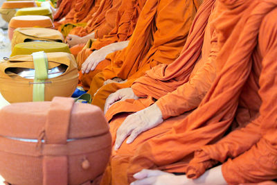 Midsection of monks sitting with containers at temple