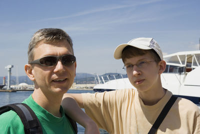 Father and son standing at harbor on sunny day against sky