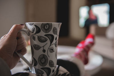 Low section of woman in warm clothing holding cup on table at home