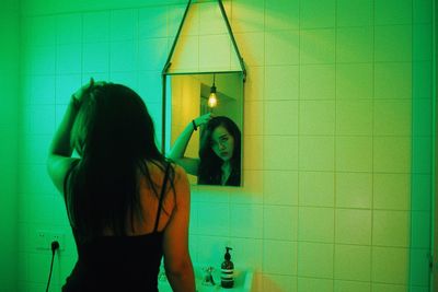 Rear view of woman standing against wall at home