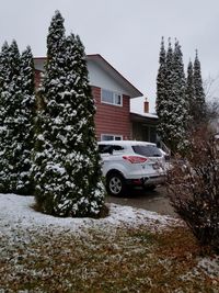Cars on snow covered field by building against sky