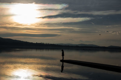 Silhouette man standing in lake against sky during sunset