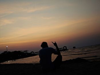 Rear view of silhouette man on beach against sky during sunset