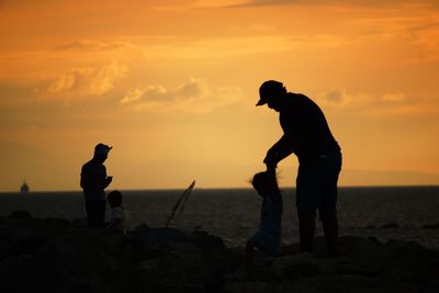 Silhouette men standing on beach against sky during sunset