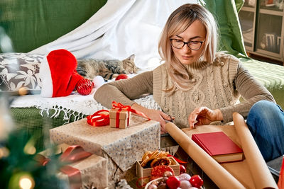 Blond woman wrapping presents in recycled card and decorated it with dried oranges and fir branches.