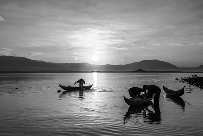 Silhouette people in lake against sky