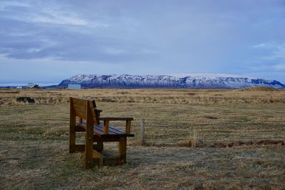 Empty bench on field against sky