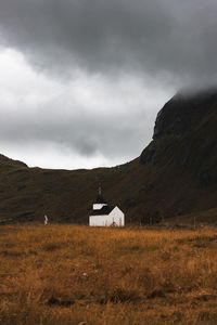 House on field by mountain against sky